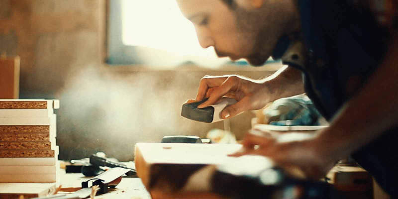 Handwerker verwendet einen Presch Schleifklotz in einer Holzwerkstatt mit weiteren Handwerkzeugen im Hintergrund
